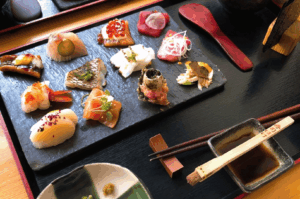 Assortment of sushi and sashimi arranged on a wooden tray with chopsticks, highlighting varied textures and precise knife work—ideal for illustrating contemporary takes on traditional omakase.