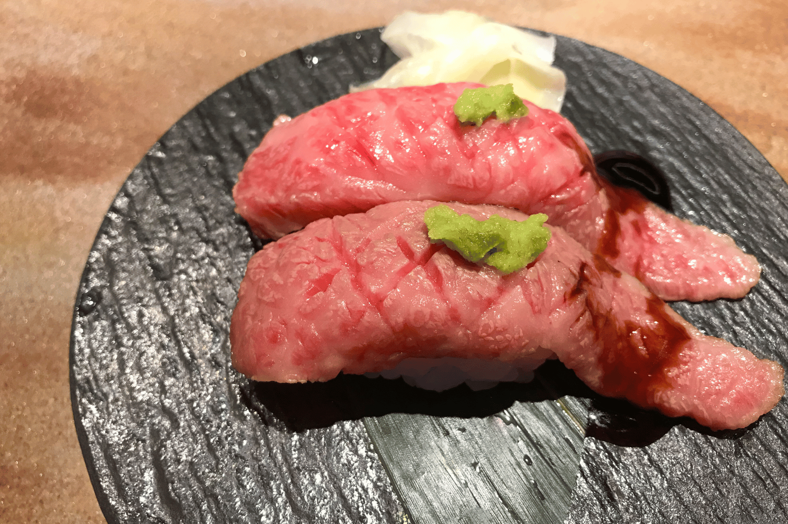 Two raw tuna steaks on a matte black plate with chopsticks, shot overhead on a dark stone surface—minimal, modern plating evokes a deconstructed sushi vibe.
