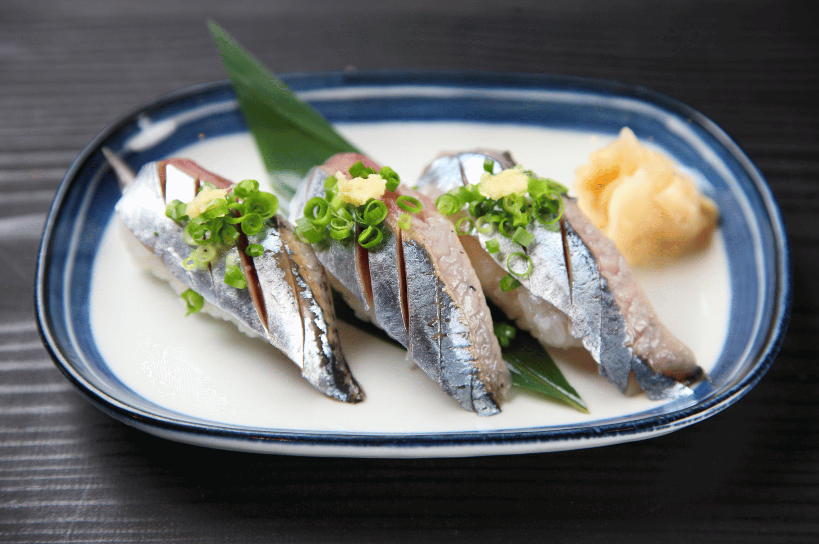 Three neatly arranged sardines on a blue-and-white plate, photographed from above—minimal, refined plating that nods to traditional technique with a modern, deconstructed presentation.