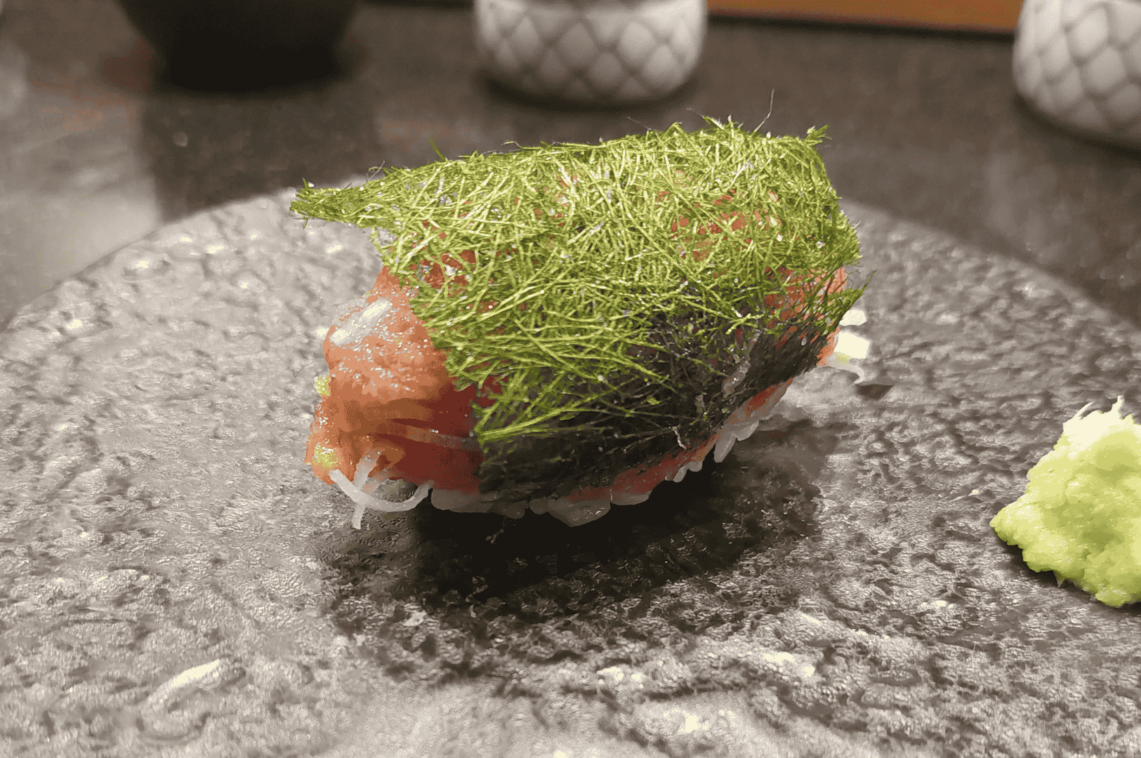 Close-up of a single piece of salmon nigiri on a black plate, spotlighted to evoke the precision and theater of premium omakase