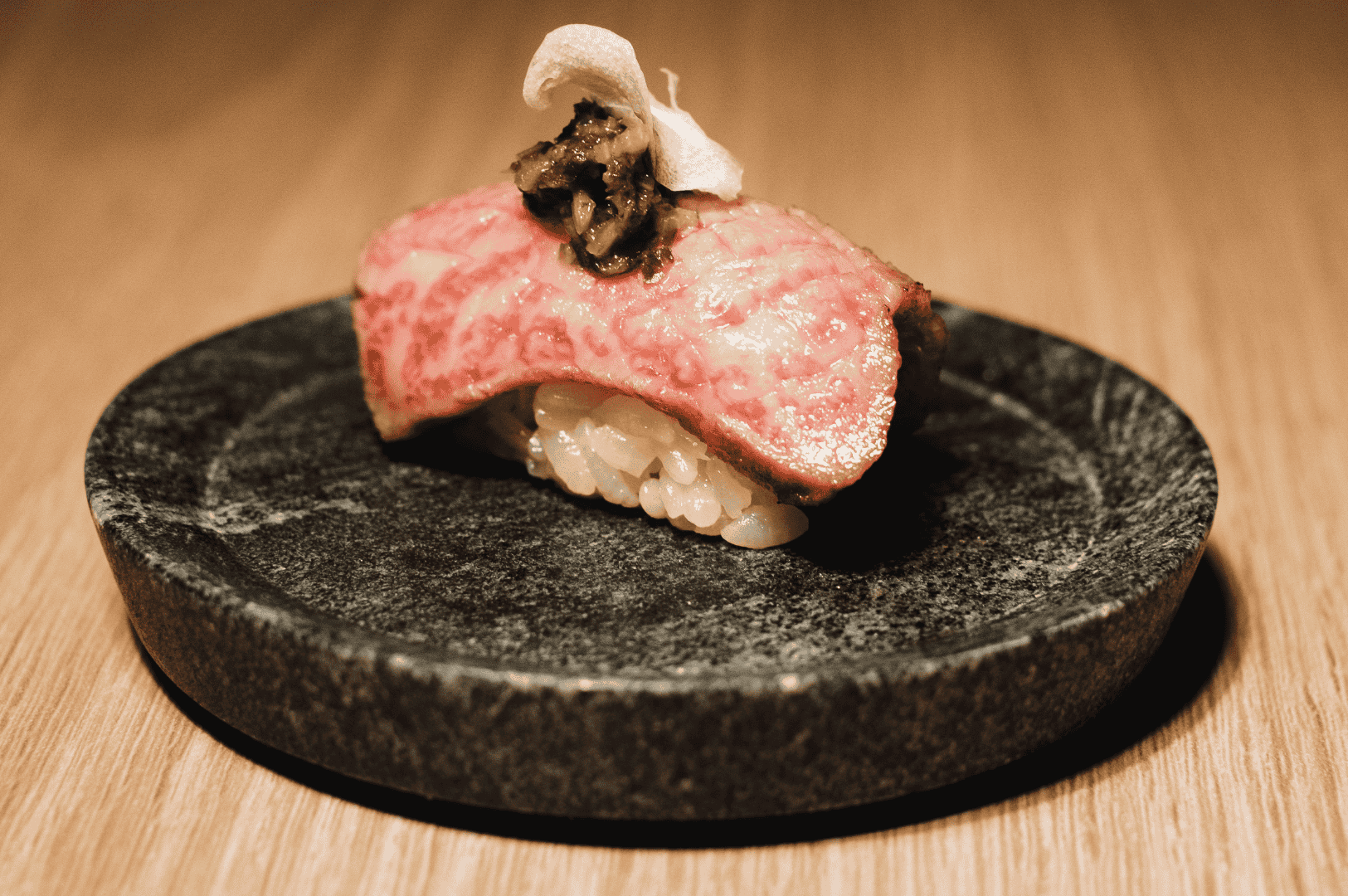 Close-up of a single nigiri on a black plate, showcasing precise fish slicing for an omakase presentation.