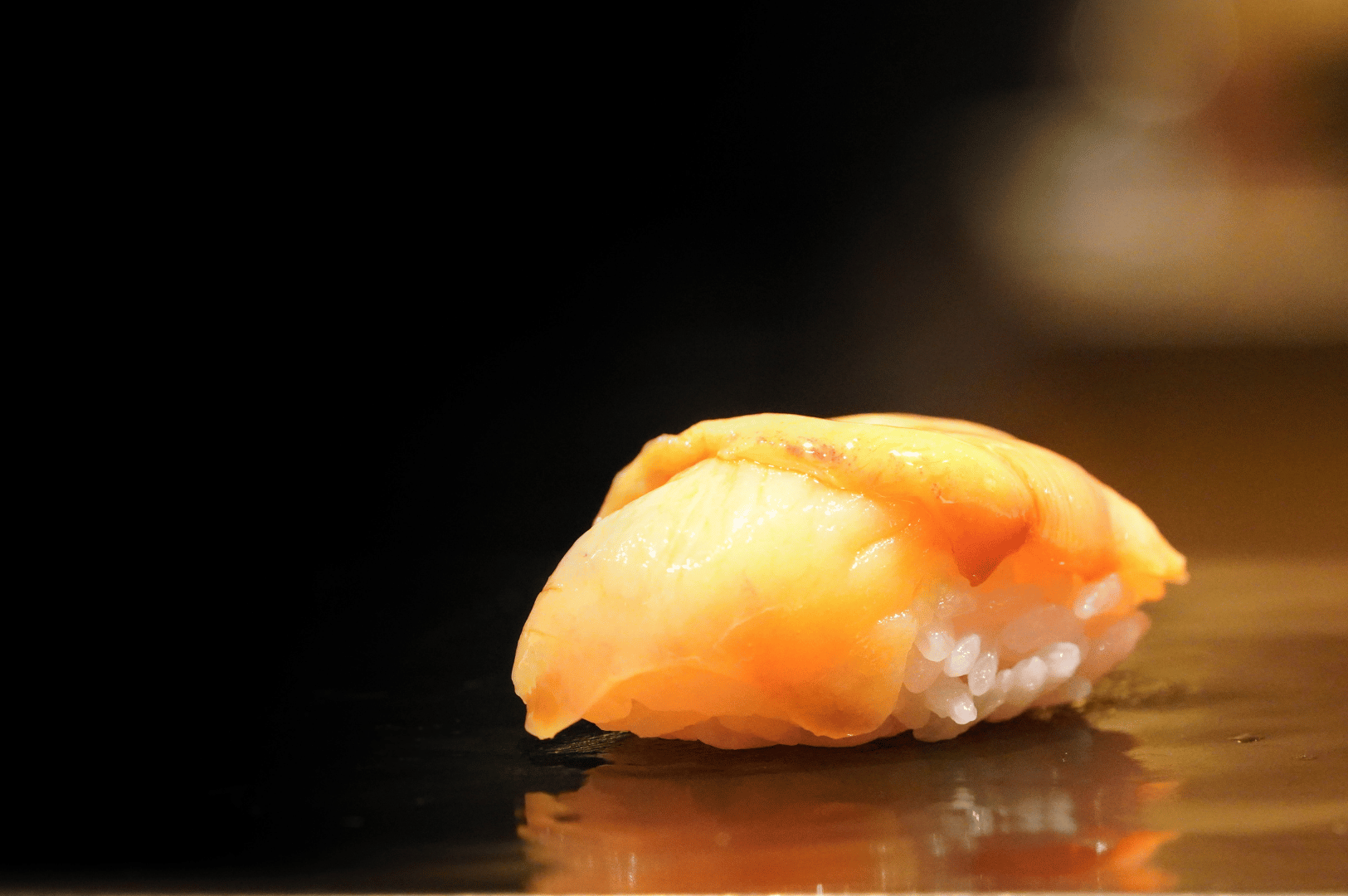 Close-up of a single nigiri sushi on a dark slate, spotlighting craftsmanship and minimal presentation for an omakase feature.