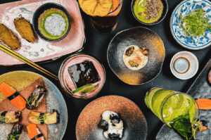 An elegant vegetarian omakase spread at a high-end Singapore restaurant, featuring artfully plated plant-based Japanese dishes in ceramic bowls and plates. The assortment includes sushi-style bites, pickled vegetables, seaweed, tofu, and vibrant garnishes, accompanied by green tea and citrus-infused drinks. The composition highlights seasonal ingredients, minimalist plating, and a harmonious balance of color and texture—capturing the essence of modern plant-based Japanese fine dining.