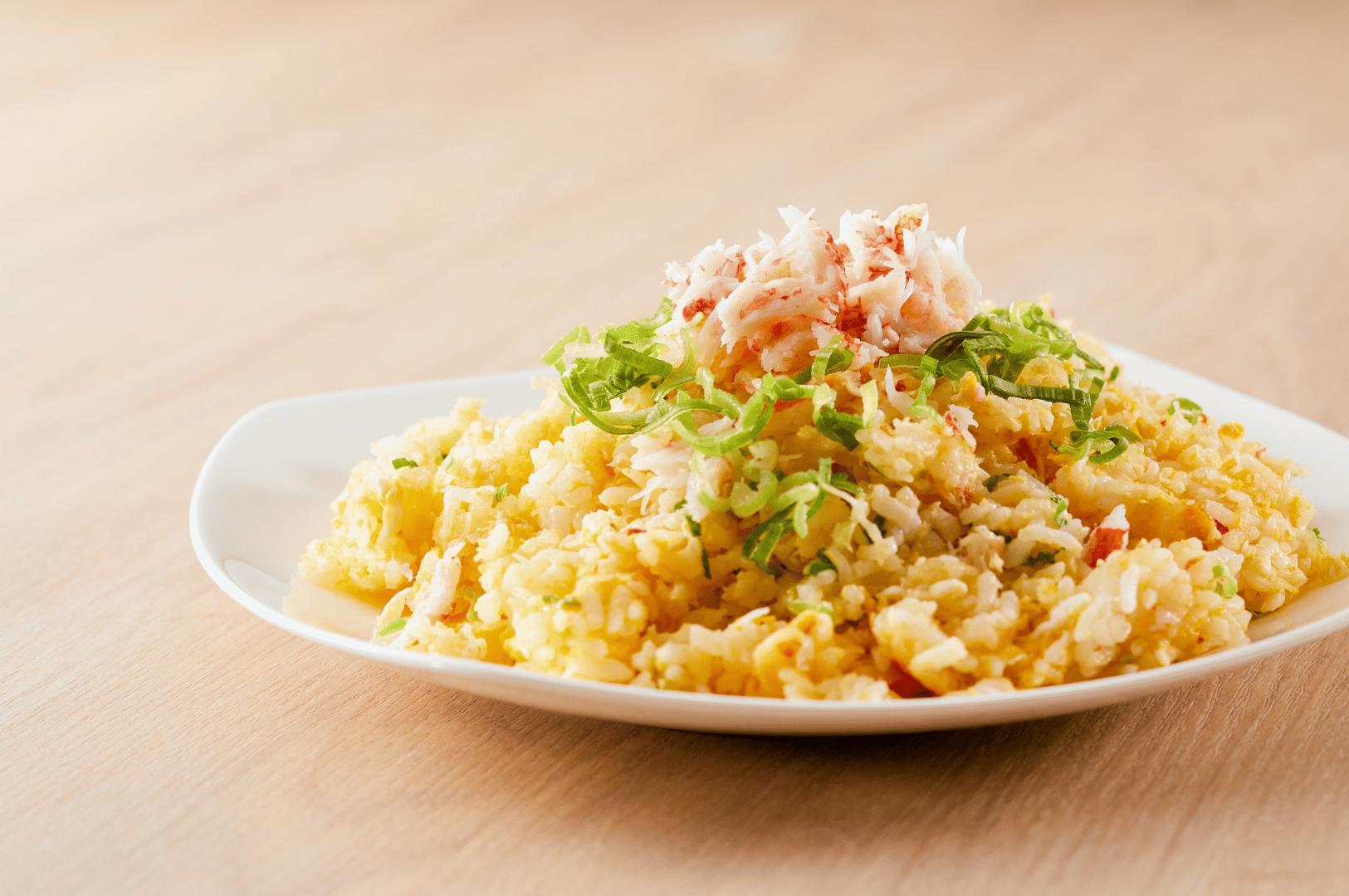 A minimalist plate of vegetarian fried rice from a Singapore omakase menu, garnished with shredded plant-based crab and chopped scallions. The rice is mixed with scrambled egg and diced vegetables, presented on a white ceramic plate atop a light wooden surface. The dish evokes comfort and refinement, blending homestyle warmth with the precision of Japanese fine dining.