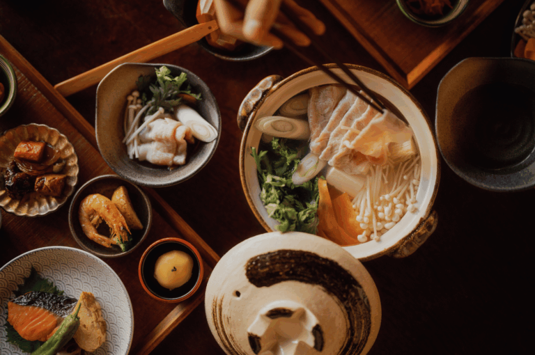 Top view of a cozy Japanese meal with hotpot, sliced fish, mushrooms, and small side dishes on a wooden table.