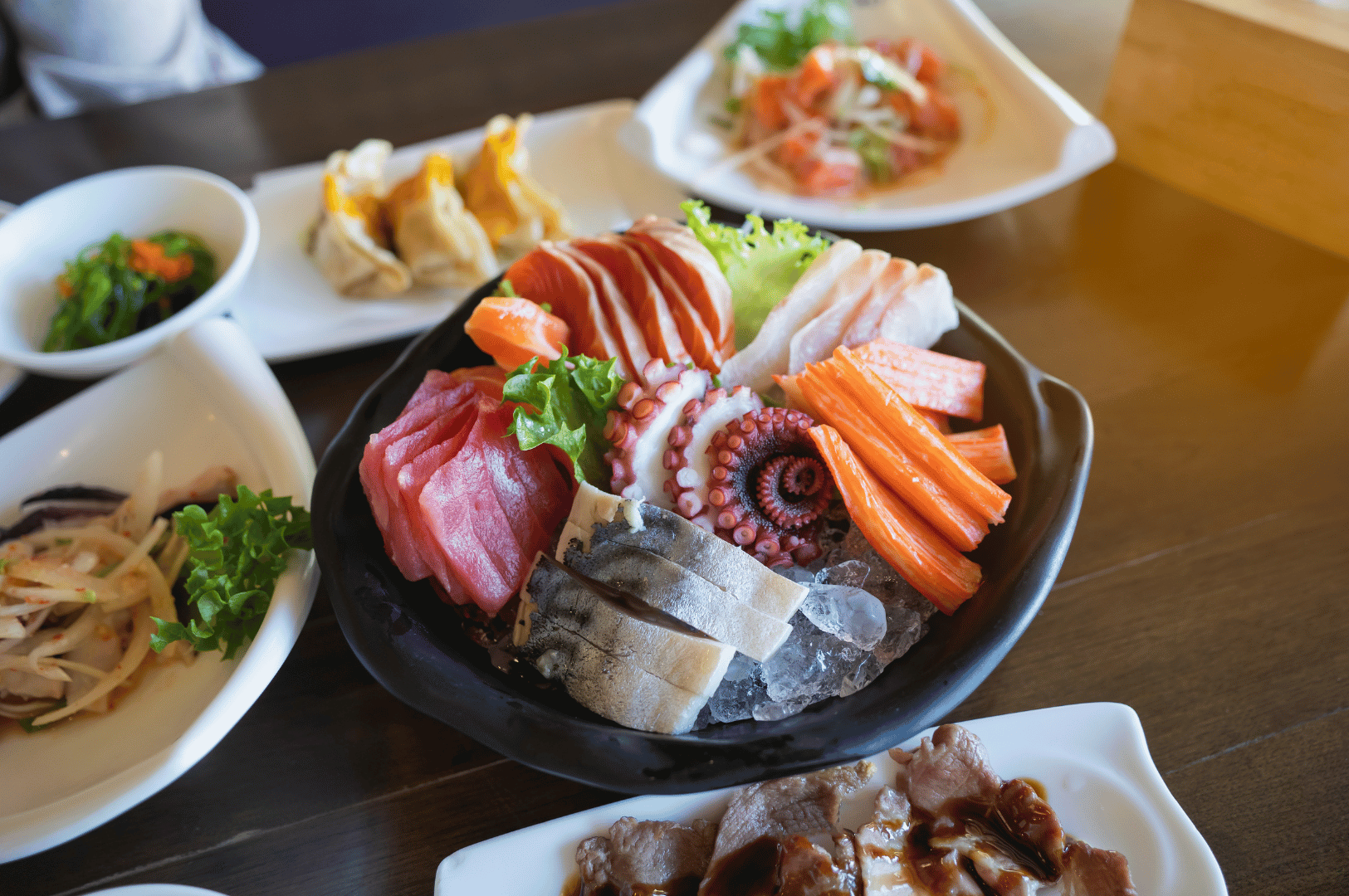 Assorted Japanese sashimi and sushi on a wooden table, including salmon, tuna, octopus, and crab sticks, with side dishes—fits article on finding Japanese food in Singapore.