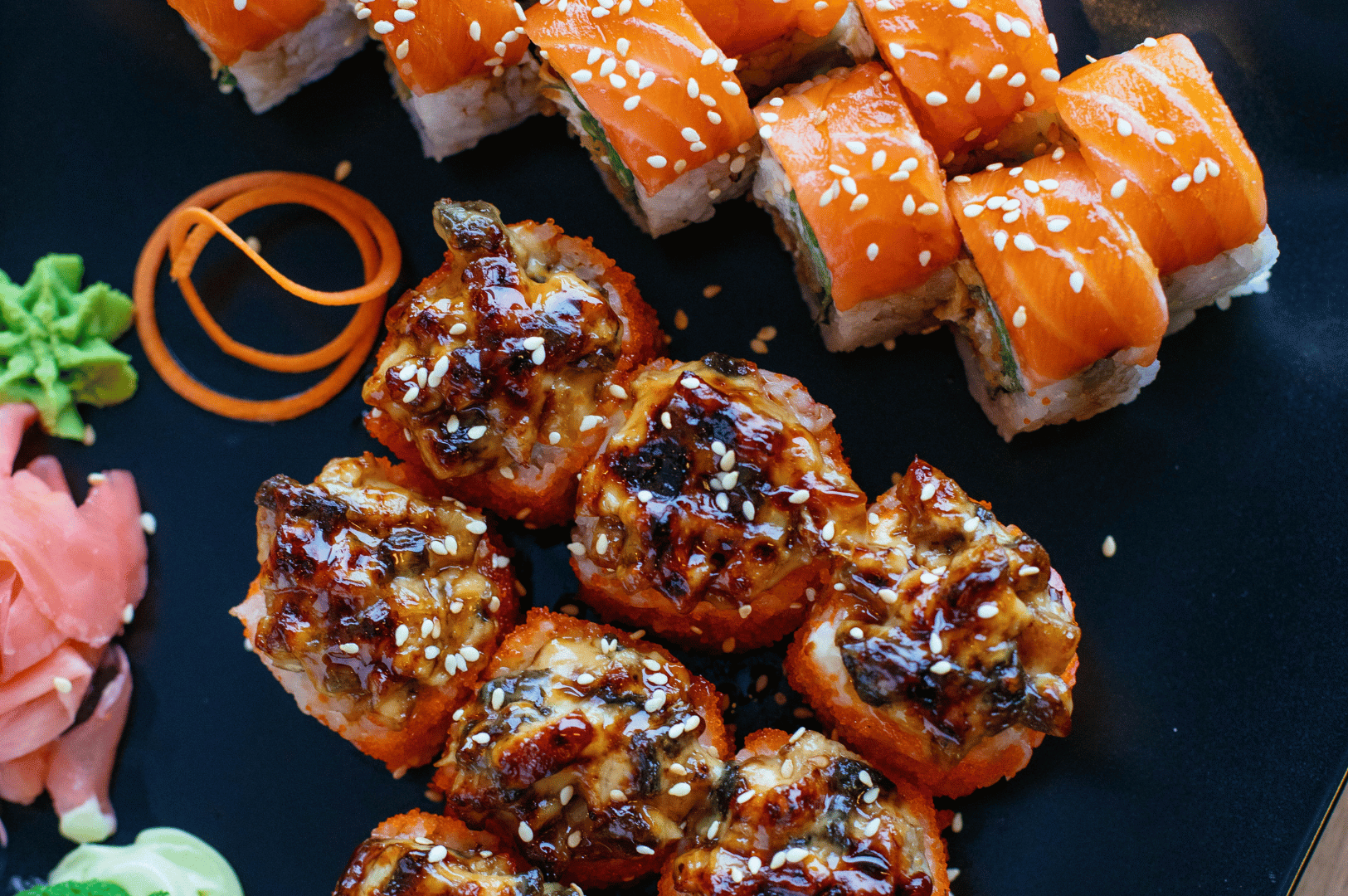 Close-up of assorted Japanese sushi rolls on a black plate with sesame seeds, pickled ginger, and wasabi, representing nearby dining options in Singapore.
