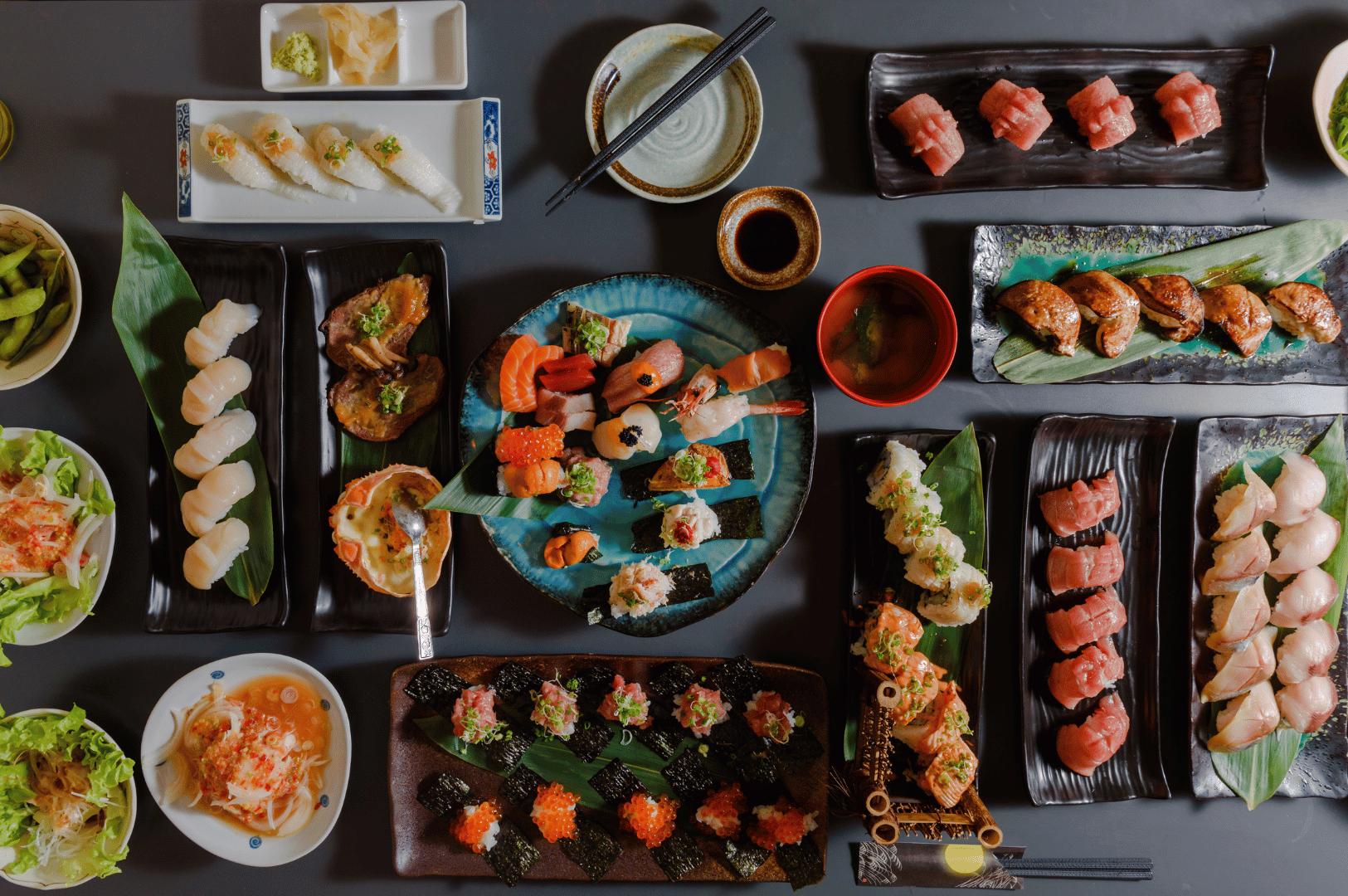 Top-down spread of assorted sushi, sashimi, and sides on a table, showing a variety of colors and textures