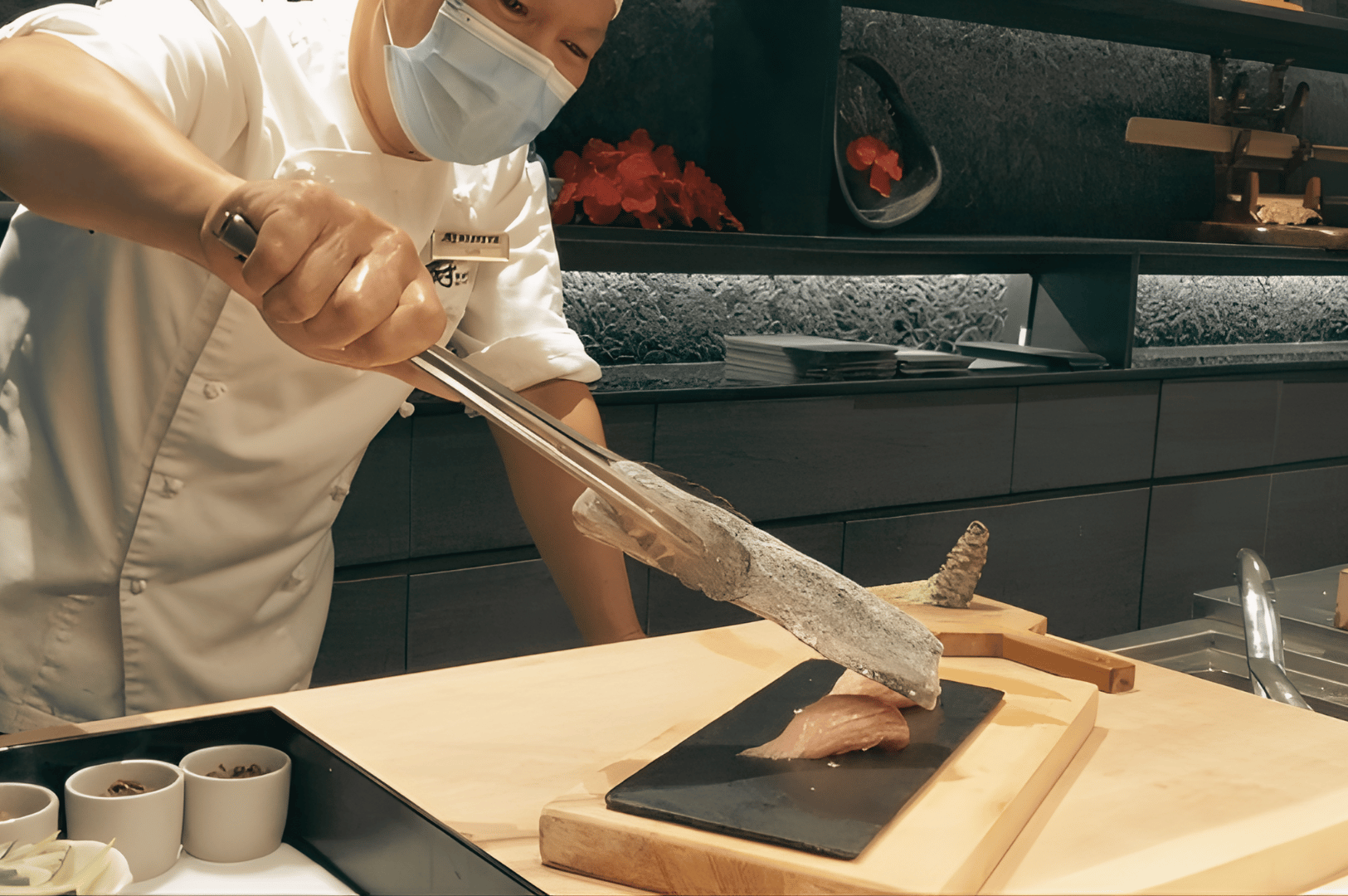 Chef at Kuriya Dining torch-searing seasonal tuna for an omakase course at the counter.