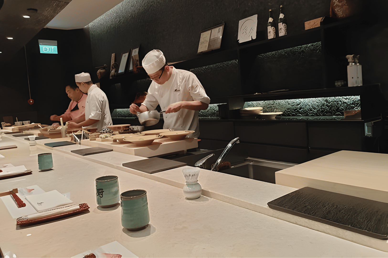 Chefs at Kuriya Dining preparing omakase courses behind a sleek counter, showcasing precise, classic Japanese techniques with seasonal ingredients.