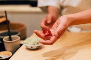 A sushi chef in a white uniform carefully presenting a piece of tuna nigiri, highlighting the artistry and precision of omakase dining at a chef’s table in Singapore.
