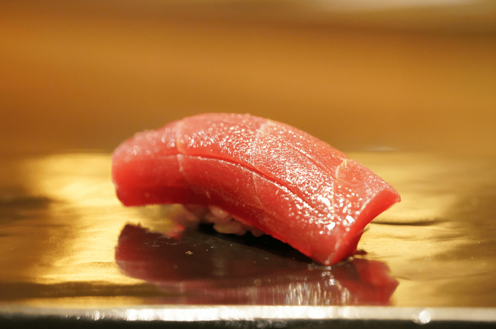 Close-up of a glistening slice of fresh tuna nigiri on vinegared rice, presented on a reflective plate, showcasing the elegance and precision of omakase sushi in Singapore.