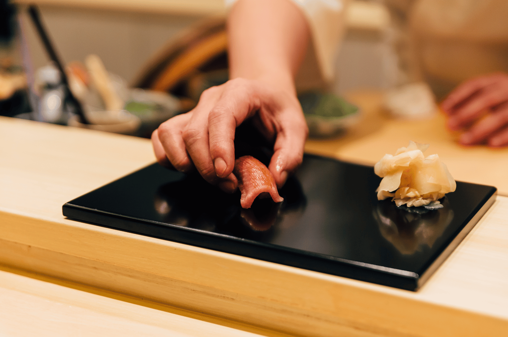 A sushi chef carefully placing a piece of tuna nigiri onto a black serving plate with pickled ginger, highlighting the precision and artistry of omakase dining in Singapore.