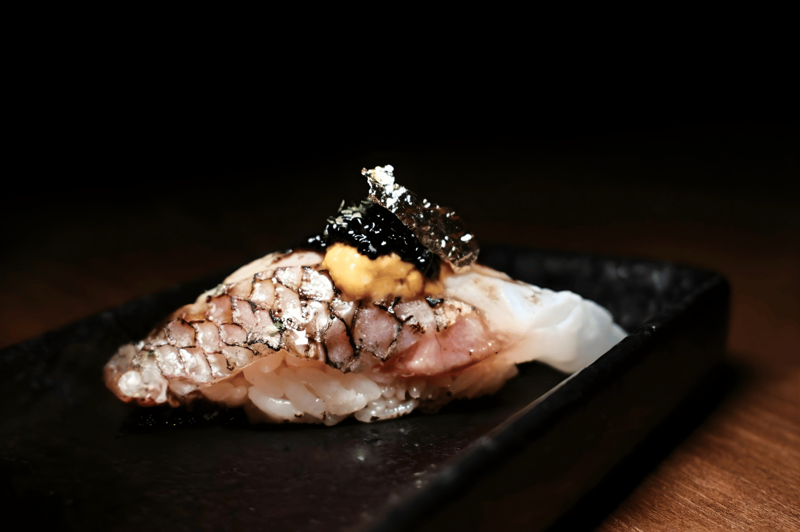 Luxurious nigiri sushi topped with seared fish, uni, caviar, and edible gold leaf on a black plate, showcasing the refined artistry of high-end omakase dining in Singapore.