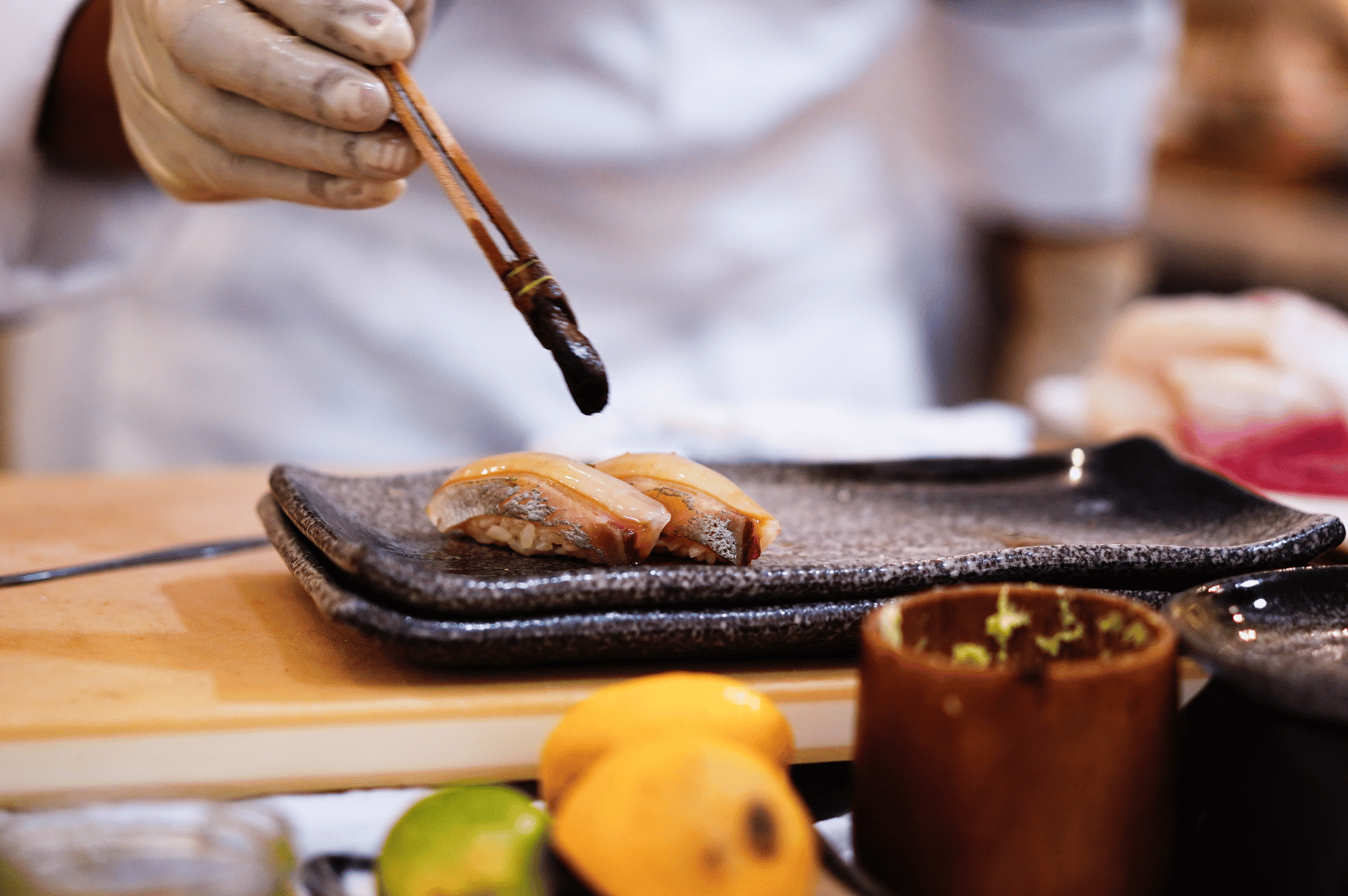 Chef applying sauce to seared sushi pieces with precision—illustrating the final touches and ingredient finesse essential to omakase preparation.