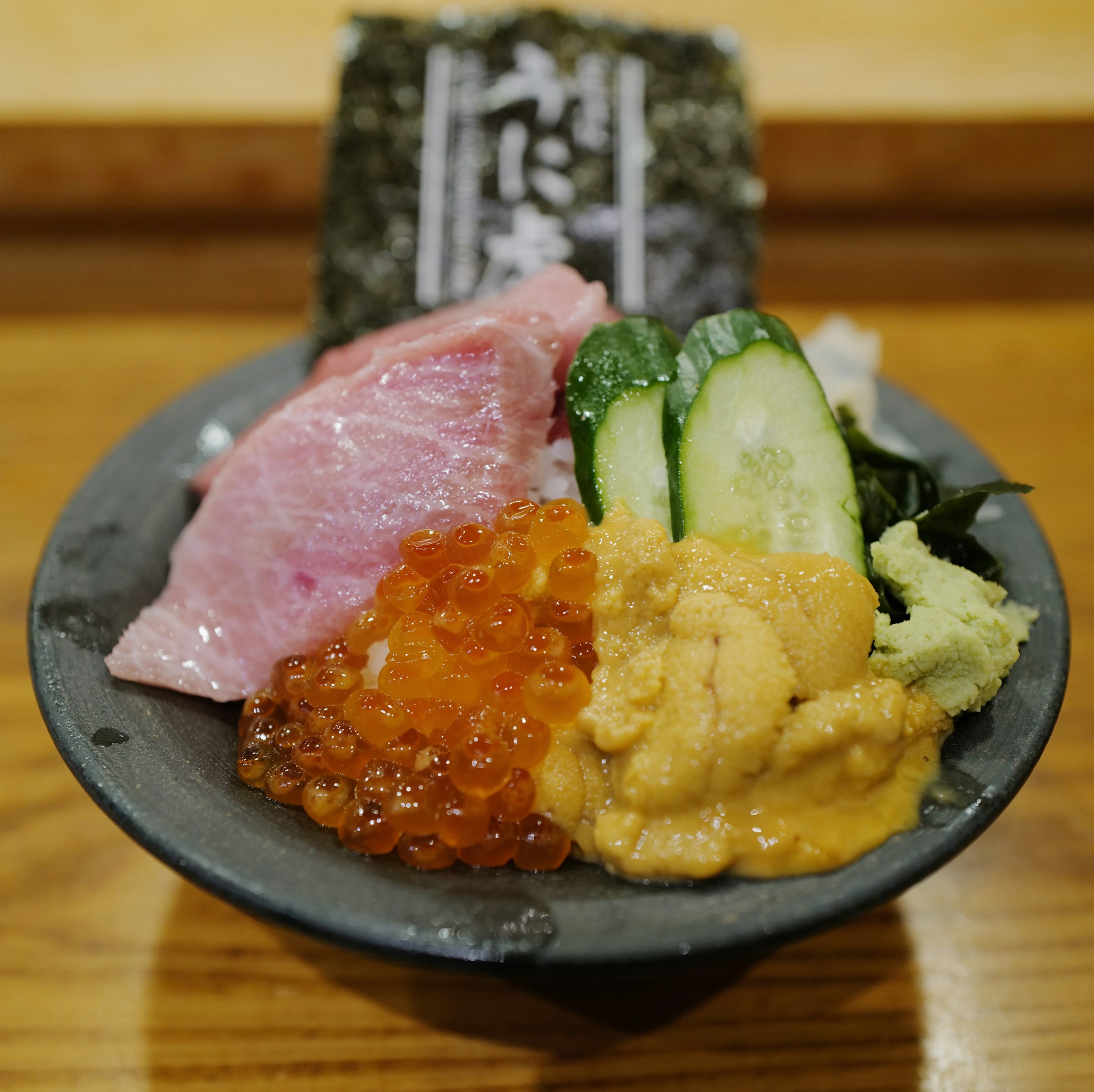 A Japanese rice bowl topped with tuna, uni, salmon roe, cucumber, and wasabi.
