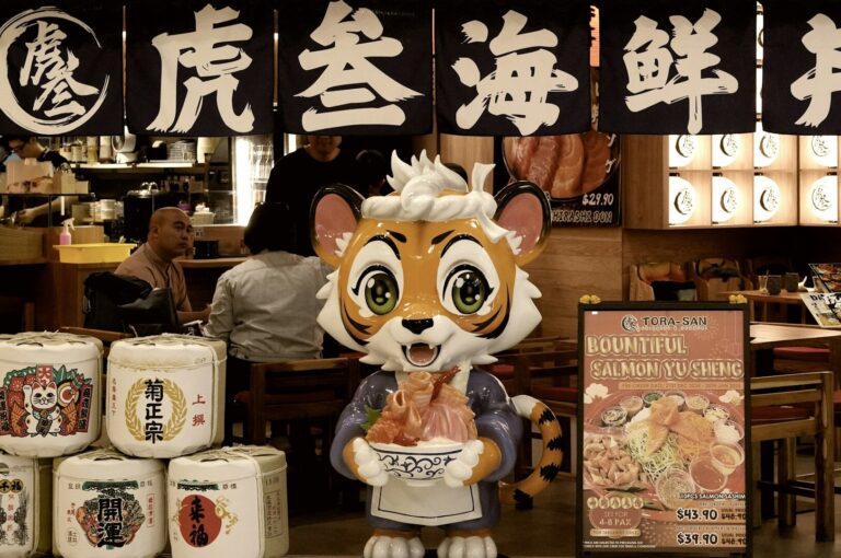 A tiger statue holding a bowl of Japanese cuisine in front of Tora-San, highlighting the dining experience in Singapore.