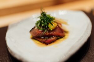 A white plate featuring a succulent piece of meat, highlighting a dish from the Ultimate Guide to Omakase in Singapore.