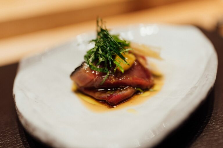 A white plate featuring a succulent piece of meat, highlighting a dish from the Ultimate Guide to Omakase in Singapore.