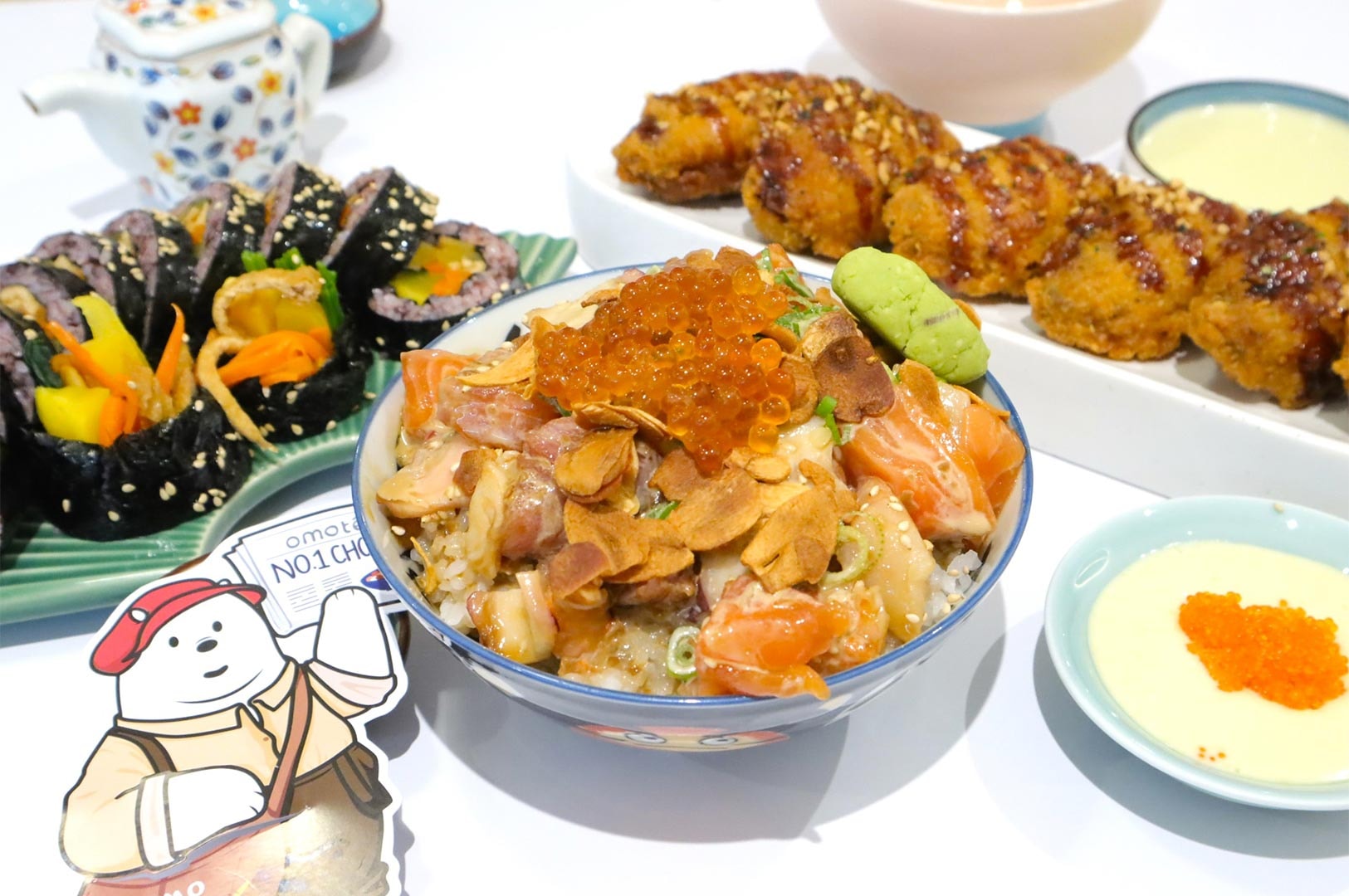 Close-up of Omote's signature chirashi don (rice bowl with mixed raw fish and ikura), next to a plate of maki sushi rolls and a dish of fried chicken.