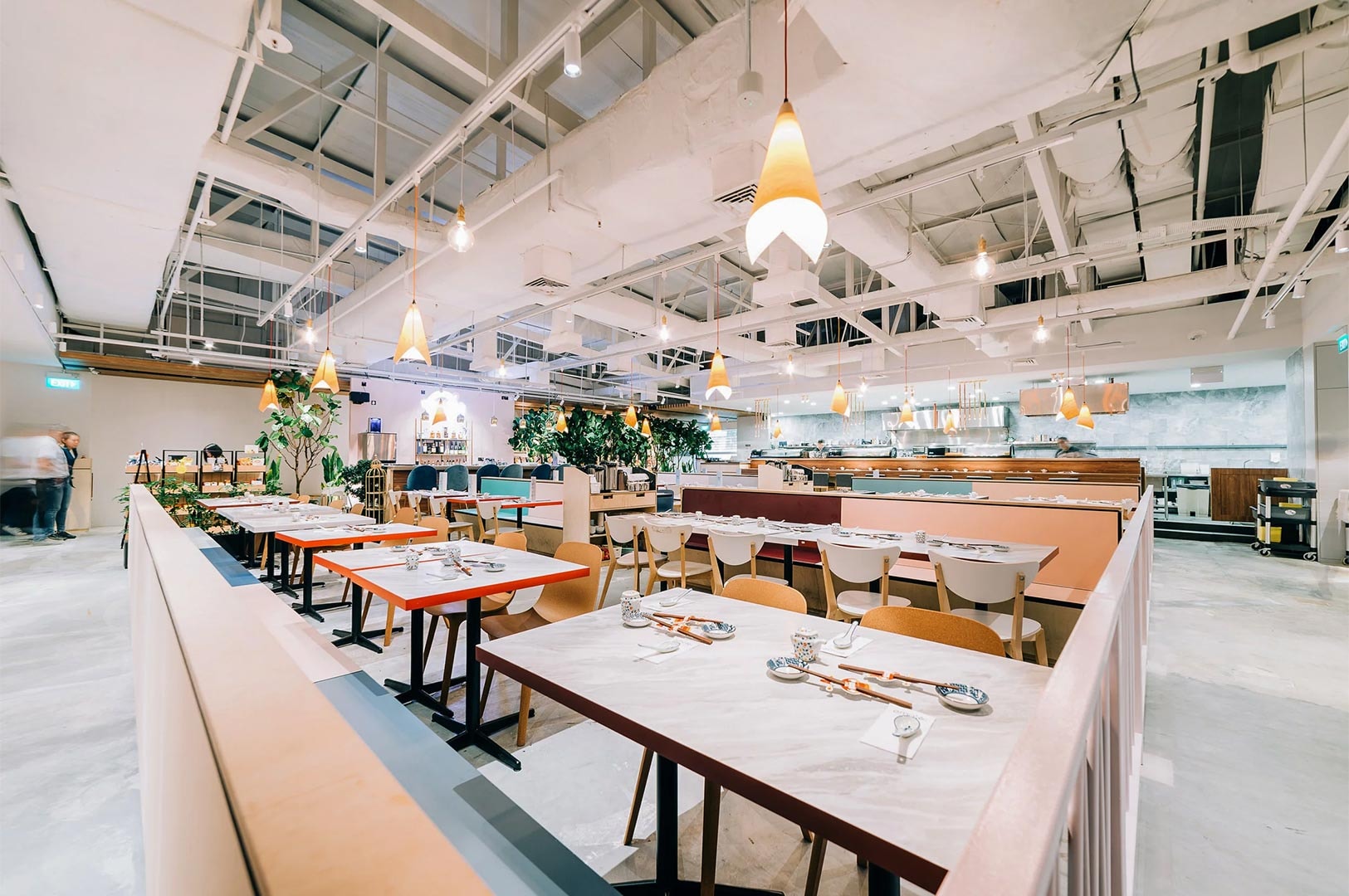 Bright, modern interior of the Omote restaurant dining hall with rows of tables, light wood accents, and distinctive orange pendant lights.