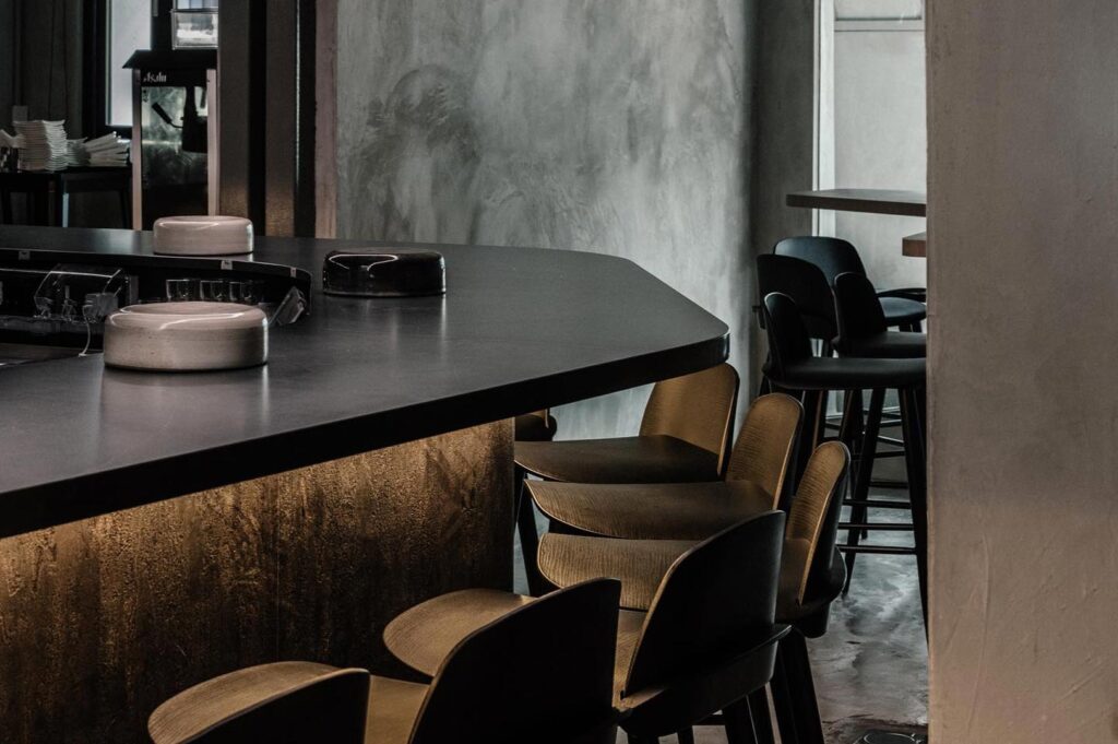 Close-up of a sleek, dark-topped sushi bar with under-counter ambient lighting and modern wooden chairs.
