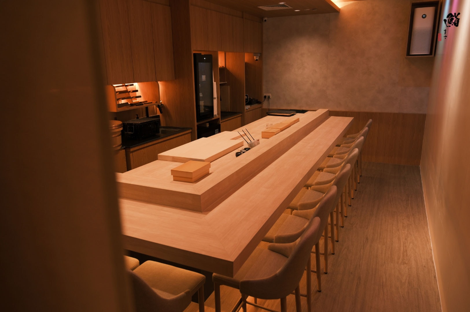 The interior of a high-end Japanese restaurant featuring a clean, minimalist wooden sushi counter and warm ambient lighting.