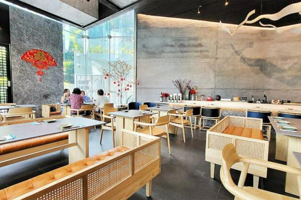 Bright, contemporary restaurant interior featuring light wood furniture, woven rattan seating, and large floor-to-ceiling windows.