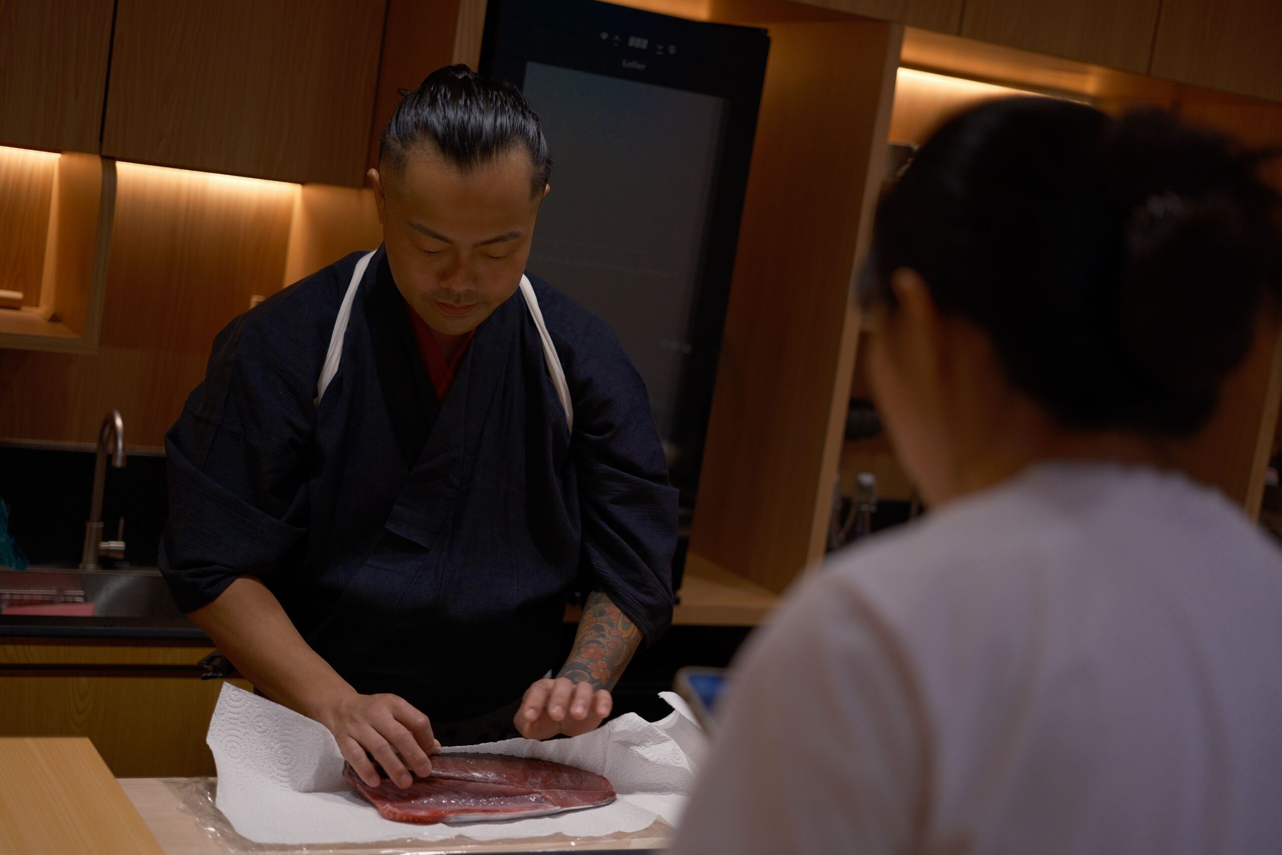 A chef at Sushi Masa by Ki-setsu skillfully prepares a piece of fish on a counter for an omakase dining experience.