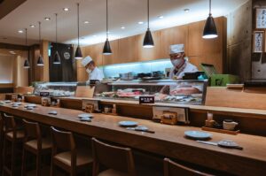 A Japanese restaurant interior featuring a long counter with a sushi chef preparing dishes for customers.
