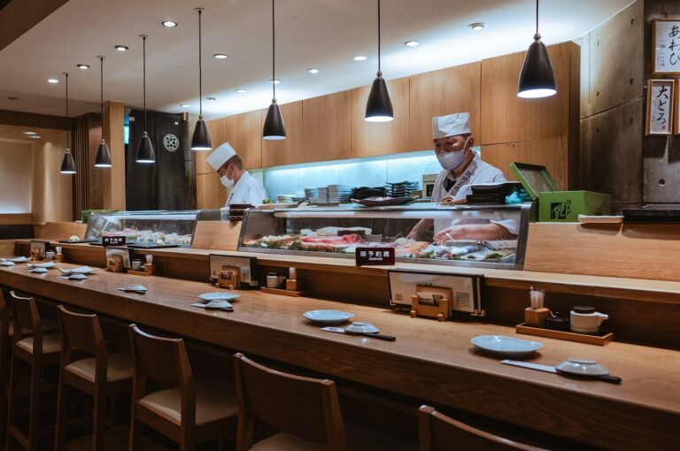 A Japanese restaurant interior featuring a long counter with a sushi chef preparing dishes for customers.
