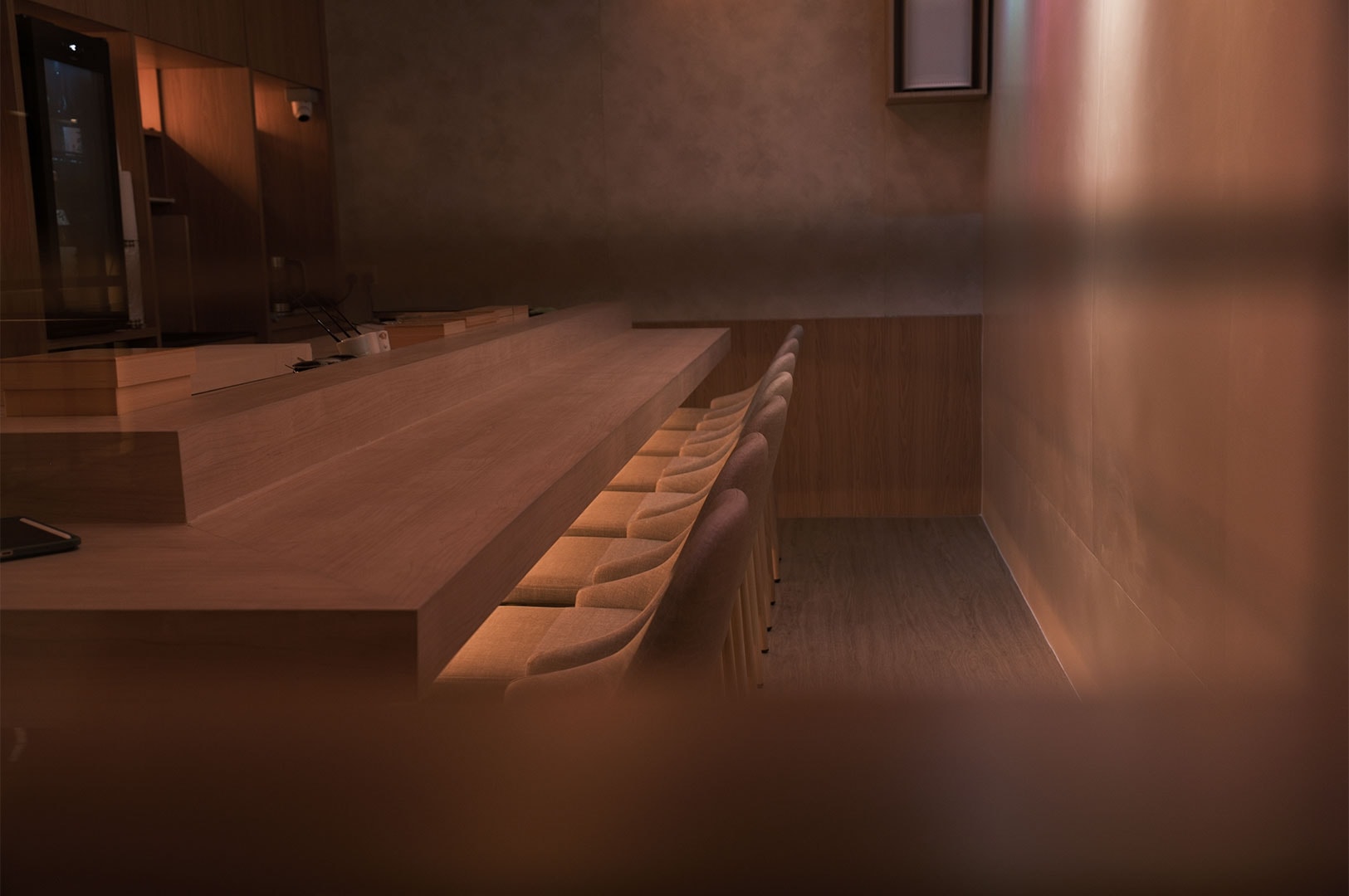 A warmly lit, empty wooden sushi counter with a row of chairs in a minimalist, high-end Japanese omakase restaurant.