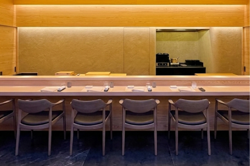 A sleek, long wooden sushi bar with glowing under-counter lighting and artistic floral wall decor in a high-end restaurant.