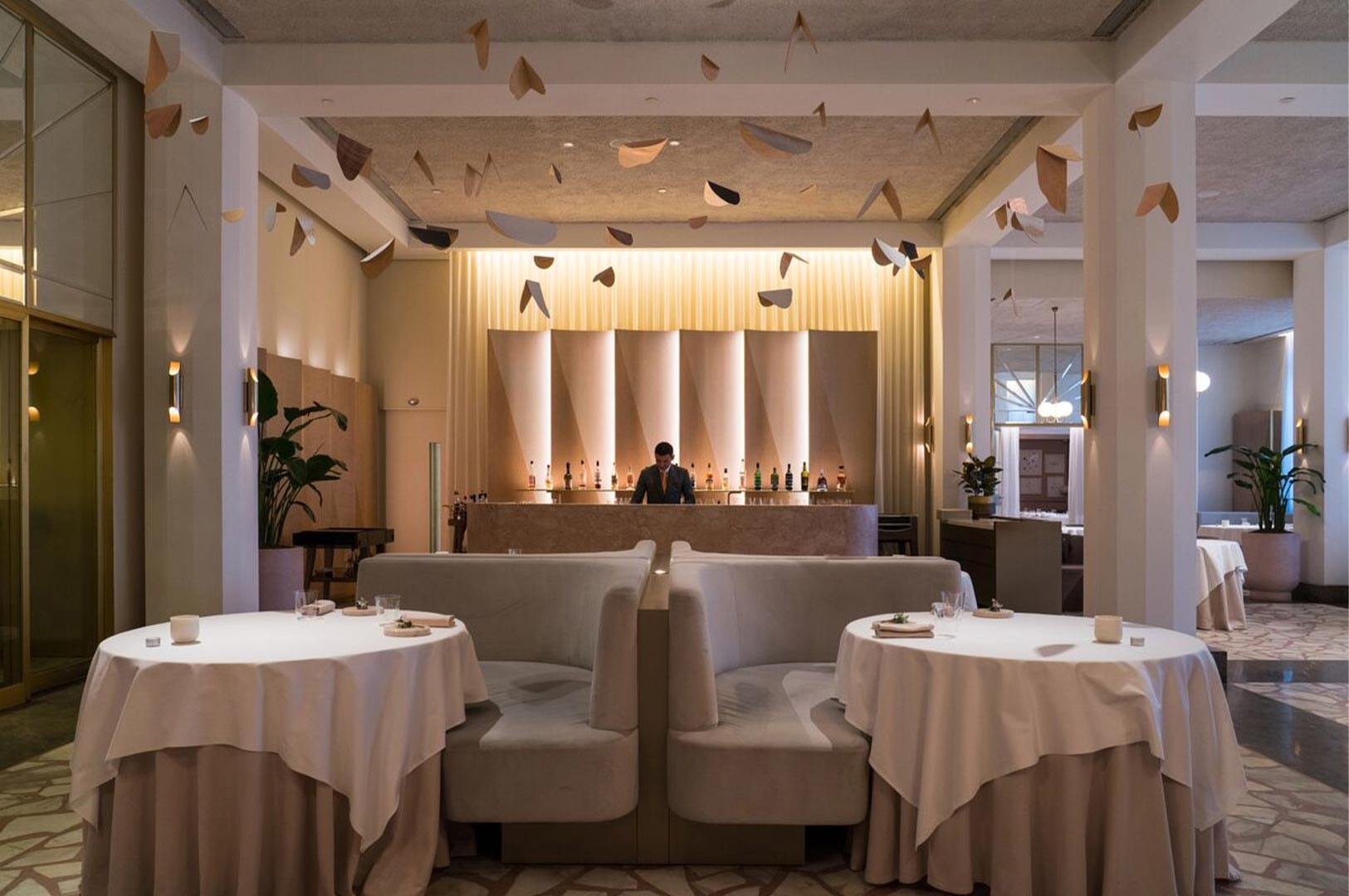 The interior of a modern, upscale restaurant featuring beige booth seating, a marble bar, and an artistic hanging ceiling installation.