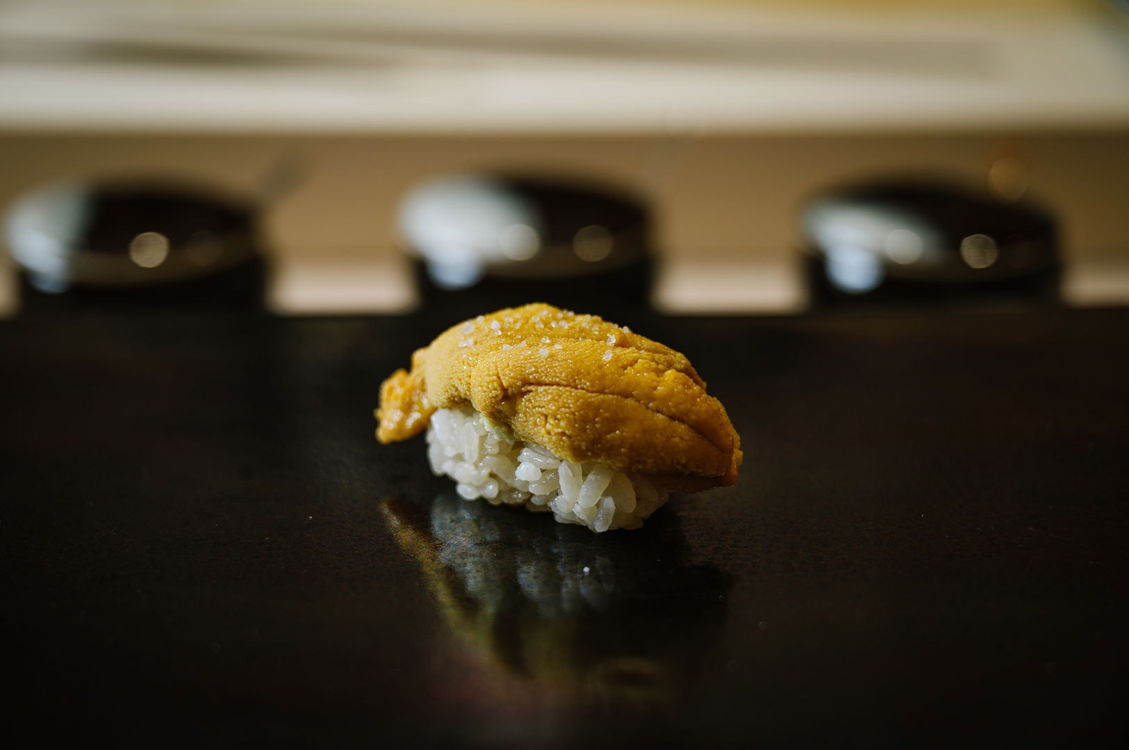 A high-resolution close-up of a fresh piece of Uni (sea urchin) nigiri sushi served on a sleek black plate.