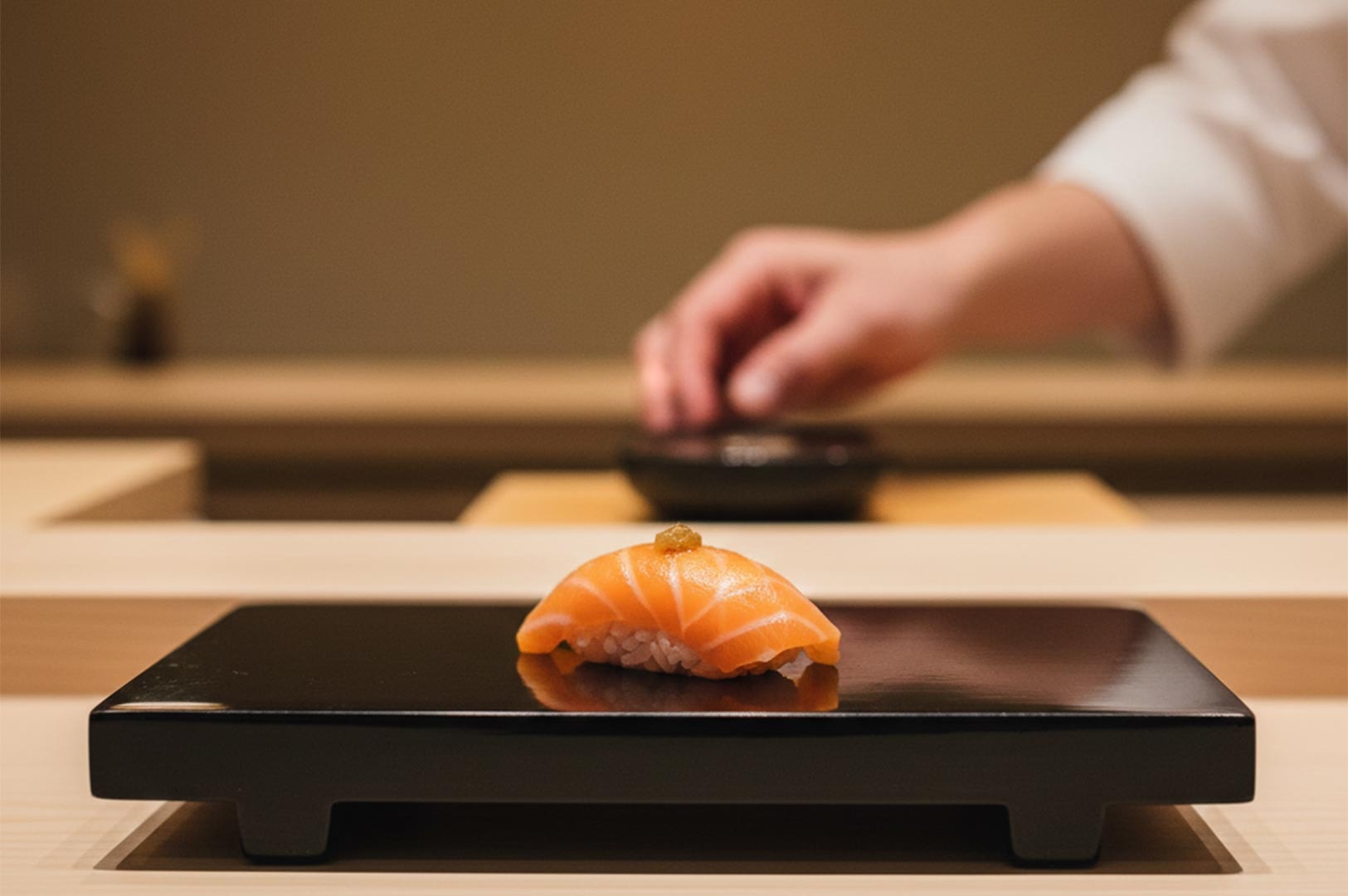 A single piece of premium salmon nigiri topped with a small garnish, served on a minimalist black lacquer raised platform at an upscale sushi bar.