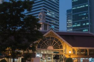 Exterior view of the historic Lau Pa Sat (Telok Ayer Market) in Singapore at night with the clock tower and surrounding skyscrapers.