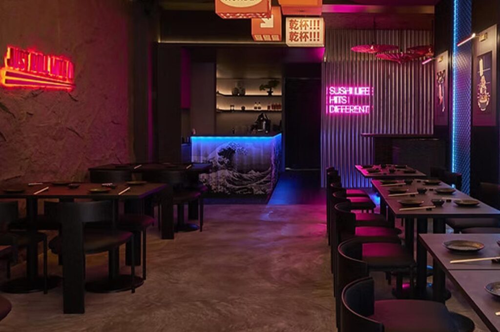 Atmospheric dining area of Shinrai restaurant with black furniture, pink neon signs, and a Great Wave off Kanagawa bar design.