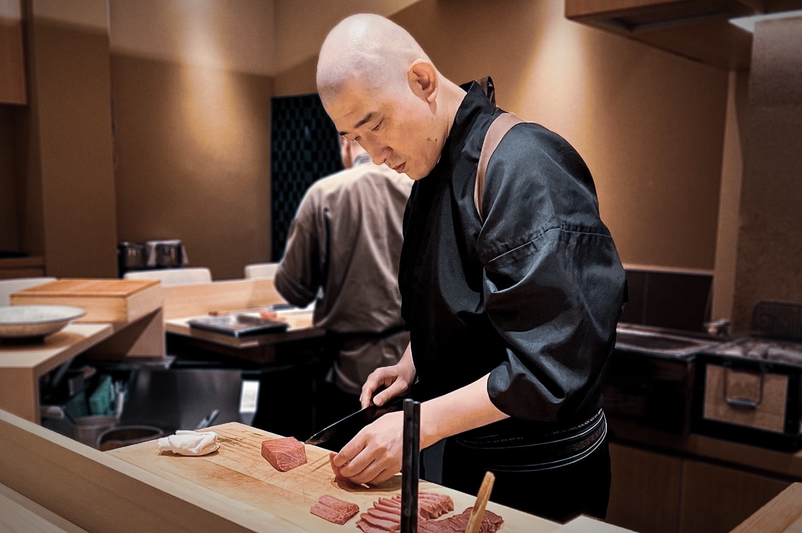Professional chef in black uniform slicing fresh tuna on cutting board at Sushi Kimura.