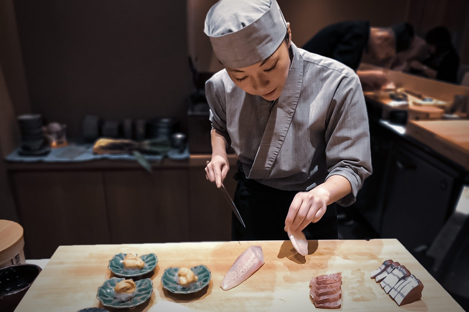 Refined sushi preparation scene with chef slicing fish and plating seafood, highlighting craftsmanship and tradition.