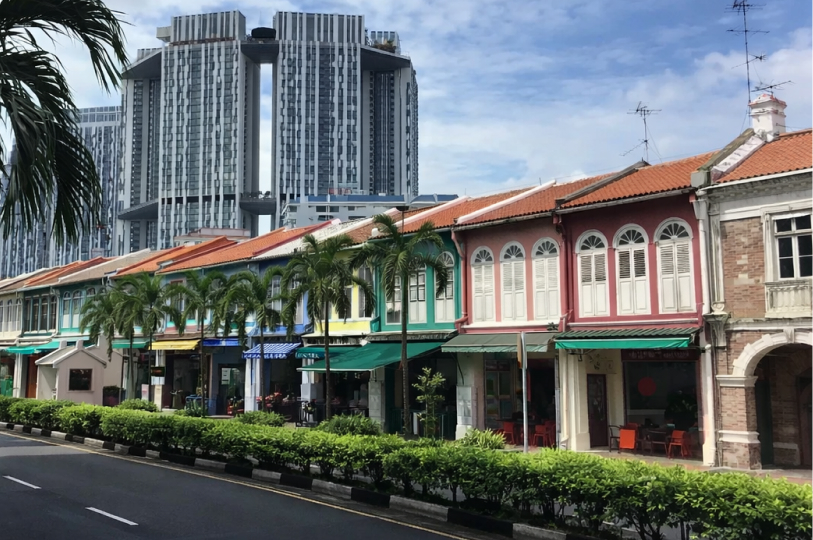 A row of colorful traditional shophouses in Tanjong Pagar, Singapore, with the modern Pinnacle@Duxton skyscraper in the background.