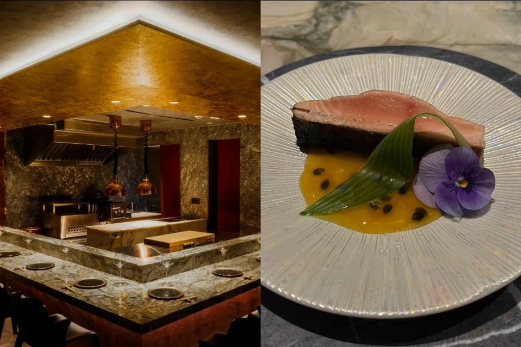 This split-screen image showcases the contrast between a luxurious dining environment and a meticulously plated dish. On the left side, a high-end Japanese omakase-style restaurant interior is visible, featuring a prominent golden recessed ceiling that casts a warm glow over a marble U-shaped counter set with elegant glassware and black plates. The background reveals a professional open kitchen with industrial exhaust hoods and hanging copper heat lamps against textured grey stone walls. The right side of the image features a close-up overhead shot of a gourmet seafood dish, consisting of a thick, seared piece of fish—possibly tuna or yellowtail—resting on a vibrant yellow passionfruit reduction speckled with seeds. The plate is pearl-white with a radial texture, garnished with a folded green leaf and a delicate purple pansy flower, emphasizing a fusion of artistic presentation and fresh ingredients.