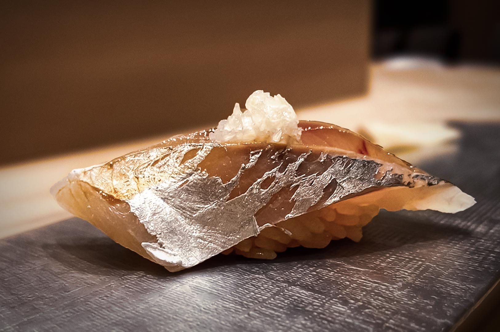 Traditional nigiri sushi with mackerel fillet and daikon garnish on vinegared rice, served on textured plate.