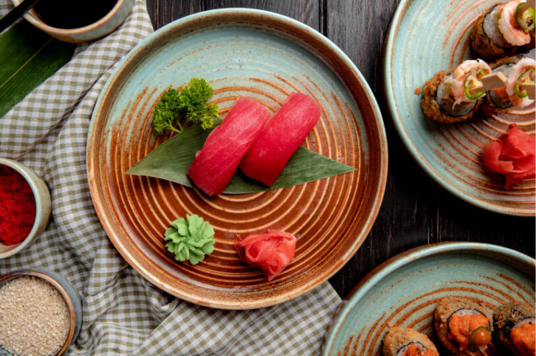 Top-down view of two pieces of tuna nigiri on a circular ceramic plate, garnished with wasabi, ginger, and parsley.