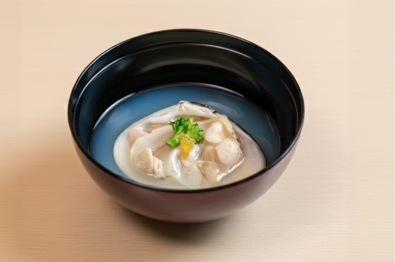 A delicate Japanese clear soup served in a black and red lacquered bowl, featuring a large poached clam garnished with greens.