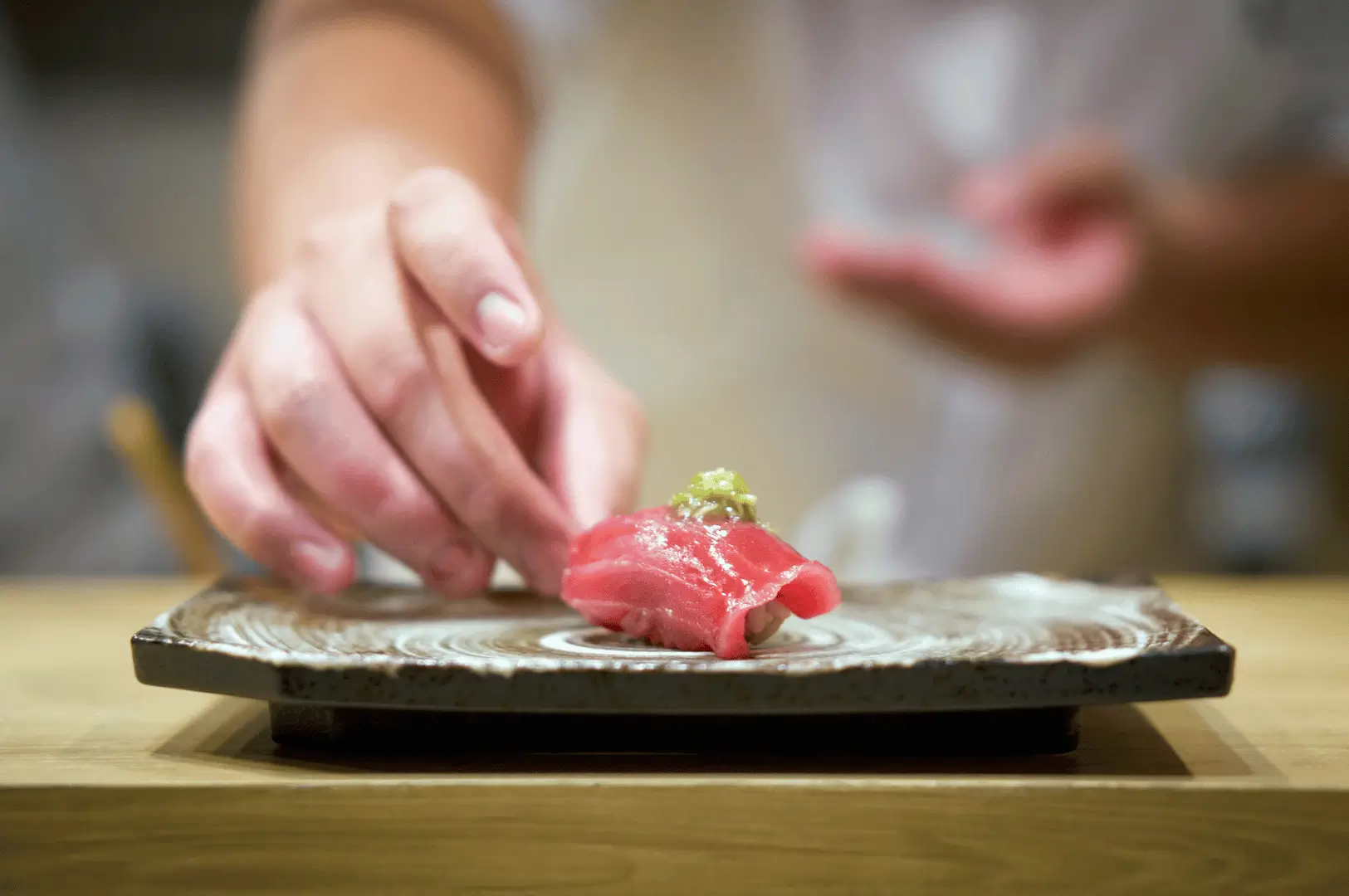 Chef placing a piece of tuna nigiri with wasabi on a decorative plate. The scene conveys precision and artistry in sushi preparation.