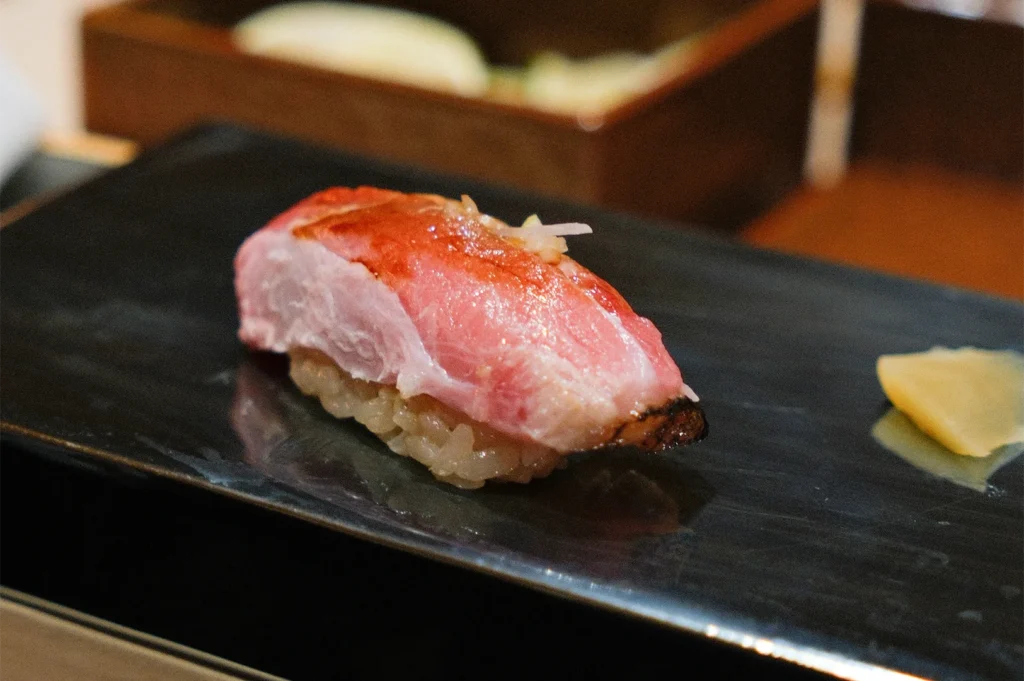 Close-up shot of a premium Otoro (fatty tuna) nigiri sushi glazed with soy sauce, served on a black stone plate.
